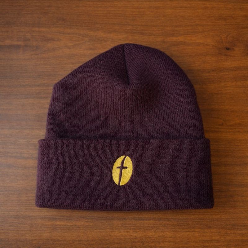 Brown beanie with a gold logo on a wood surface