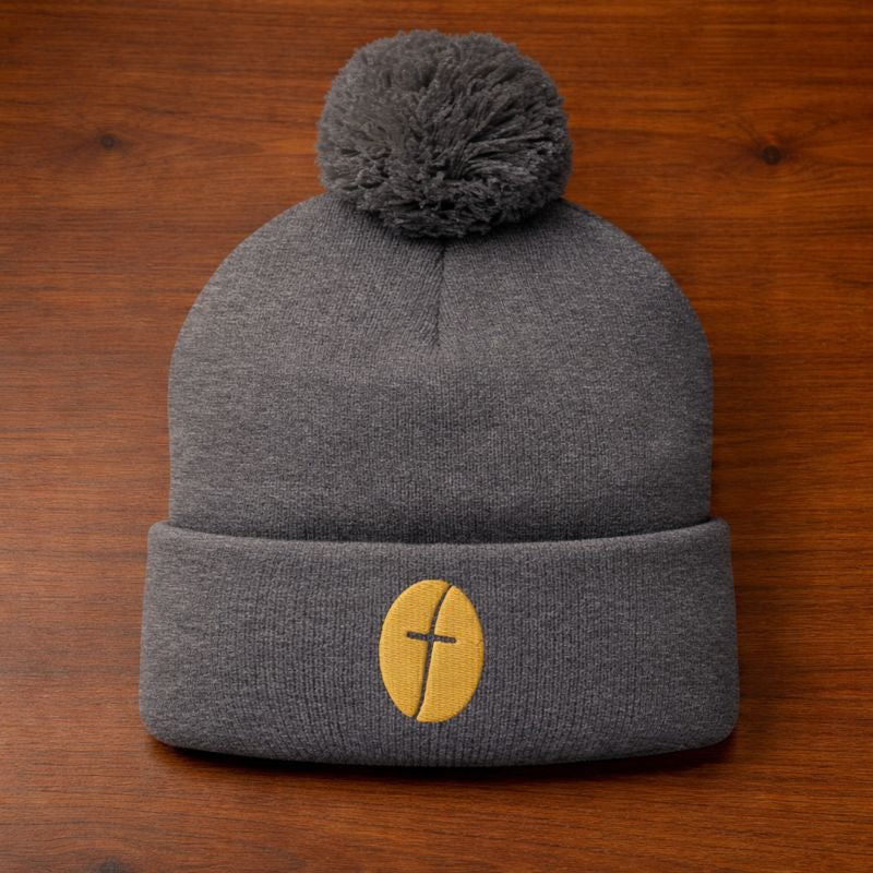 Gray beanie with a pom-pom and yellow logo on a wooden surface